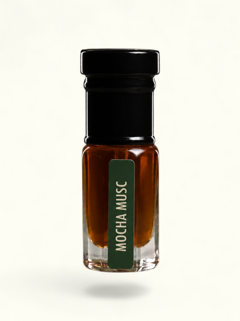 A small clear glass bottle filled with amber-brown liquid, topped with a black cap, and featuring a dark green vertical label that reads 'MOCHA MUSC' in white text, centered on a plain off-white background.