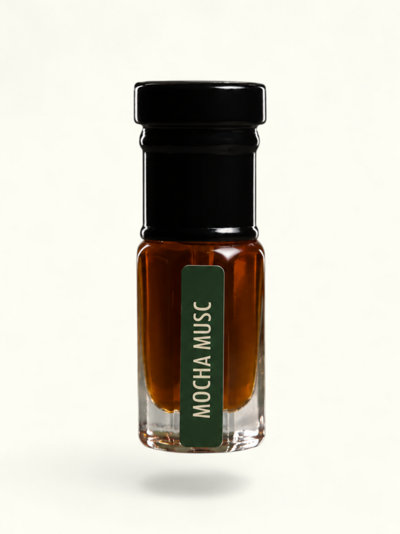 A small clear glass bottle filled with amber-brown liquid, topped with a black cap, and featuring a dark green vertical label that reads 'MOCHA MUSC' in white text, centered on a plain off-white background.