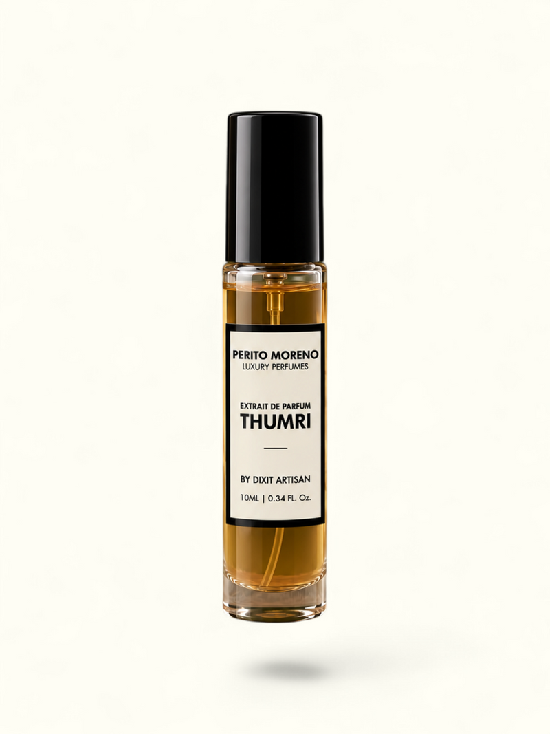 A clear glass rollerball perfume bottle filled with amber liquid, featuring a black cap and a white label that reads 'Presto Morando' and 'Thumri'. The bottle is displayed on a rustic stone slab against a solid olive green background.