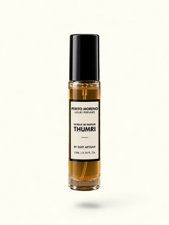 A clear glass rollerball perfume bottle filled with amber liquid, featuring a black cap and a white label that reads 'Presto Morando' and 'Thumri'. The bottle is displayed on a rustic stone slab against a solid olive green background.