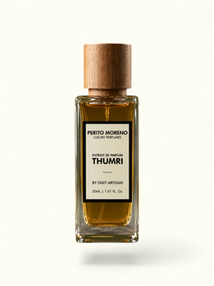 A rectangular glass perfume bottle filled with amber liquid, topped with a natural wood cap, standing on a rough stone slab against an olive green background. The front label reads Perito Moreno Scents Thumri.