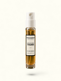 A clear glass perfume spray bottle with amber liquid and a white pump, standing on a rough stone slab against an olive green background. The front label reads Ferito Moreno Thumri.